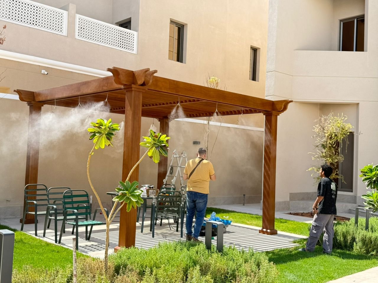 جلسة خارجية بفلة سكنية مع خط ضباب على البرجولة ومسطح أخضر ونباتات محيطة